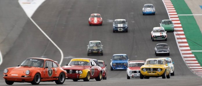 Algarve-Classic-Cars Descrição atualizada: Um grupo de pequenos carros num autódromo com a 'M80 Rádio' no Algarve Classic Festival em Portimão.